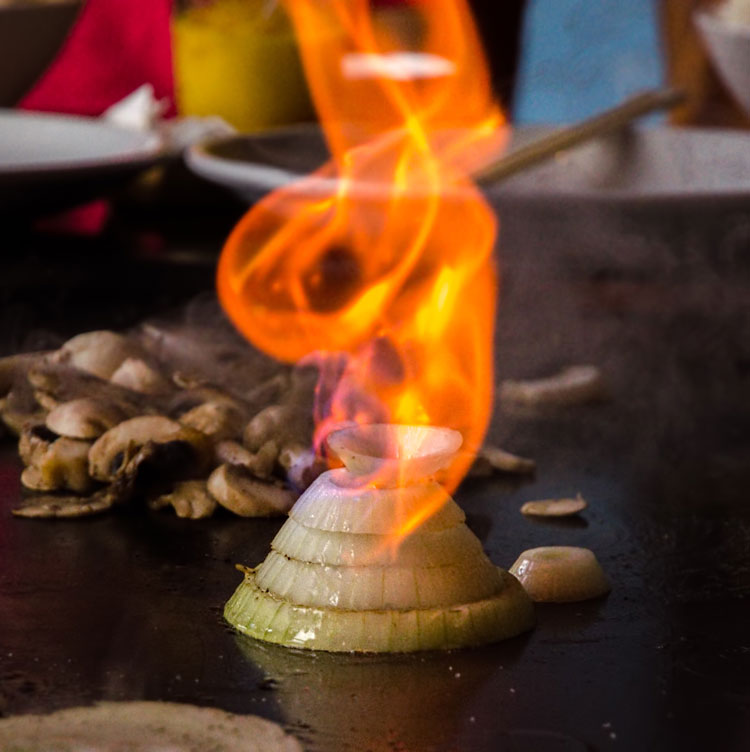 Close up of an onion on a grill sliced to look like a volcano with flames on it.